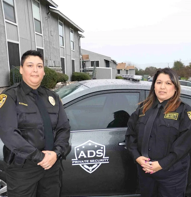 Two security officers standing next to American Discount Security (A.D.S.) Private Security vehicle in front of a building, providing safety services.