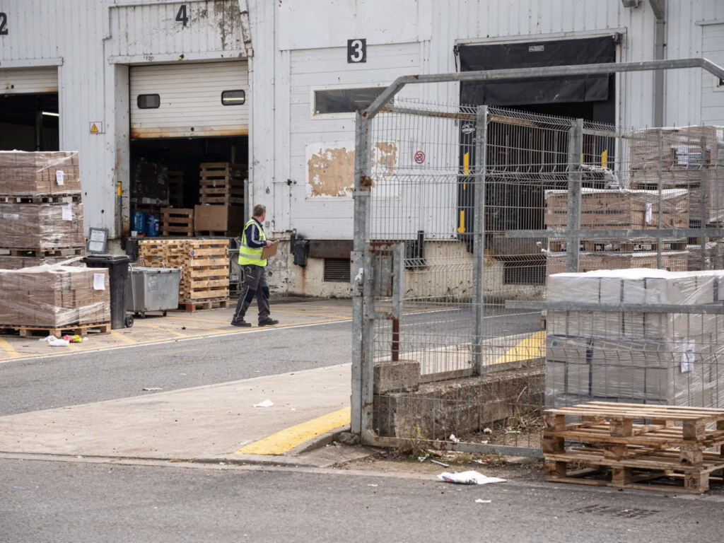 A site manager inspecting loading docks, fenced storage areas, pallets, and delivery access points.