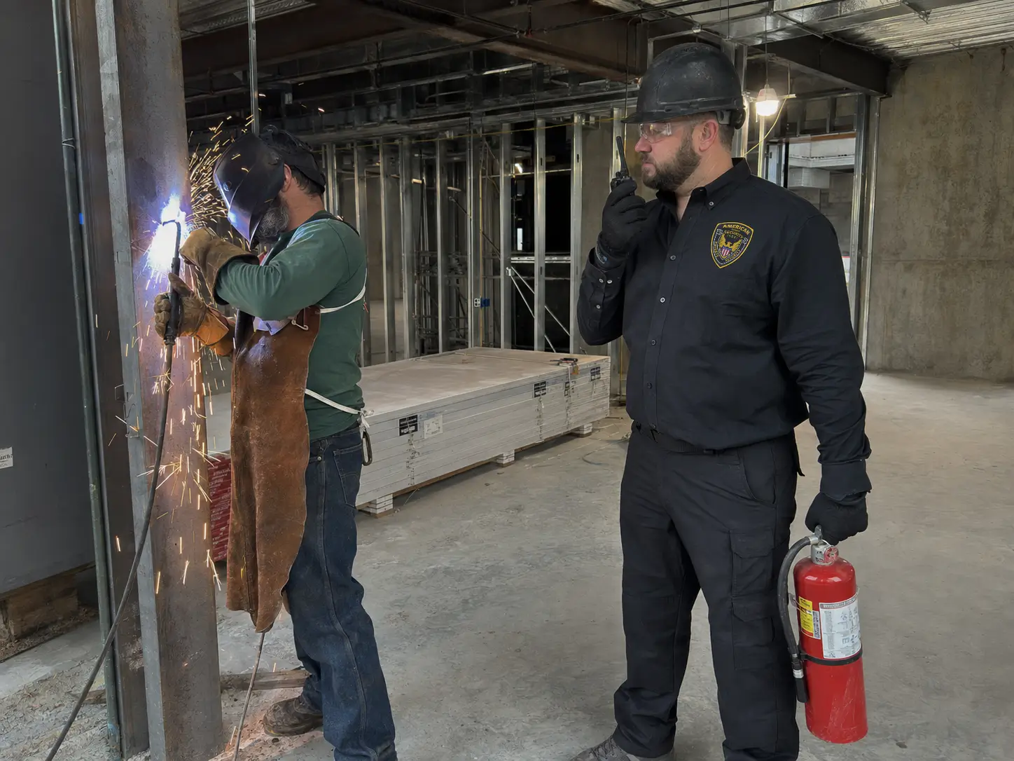 ADS Security Guards fire watch officer monitors a welder and keeps a fire extinguisher ready during hot work.